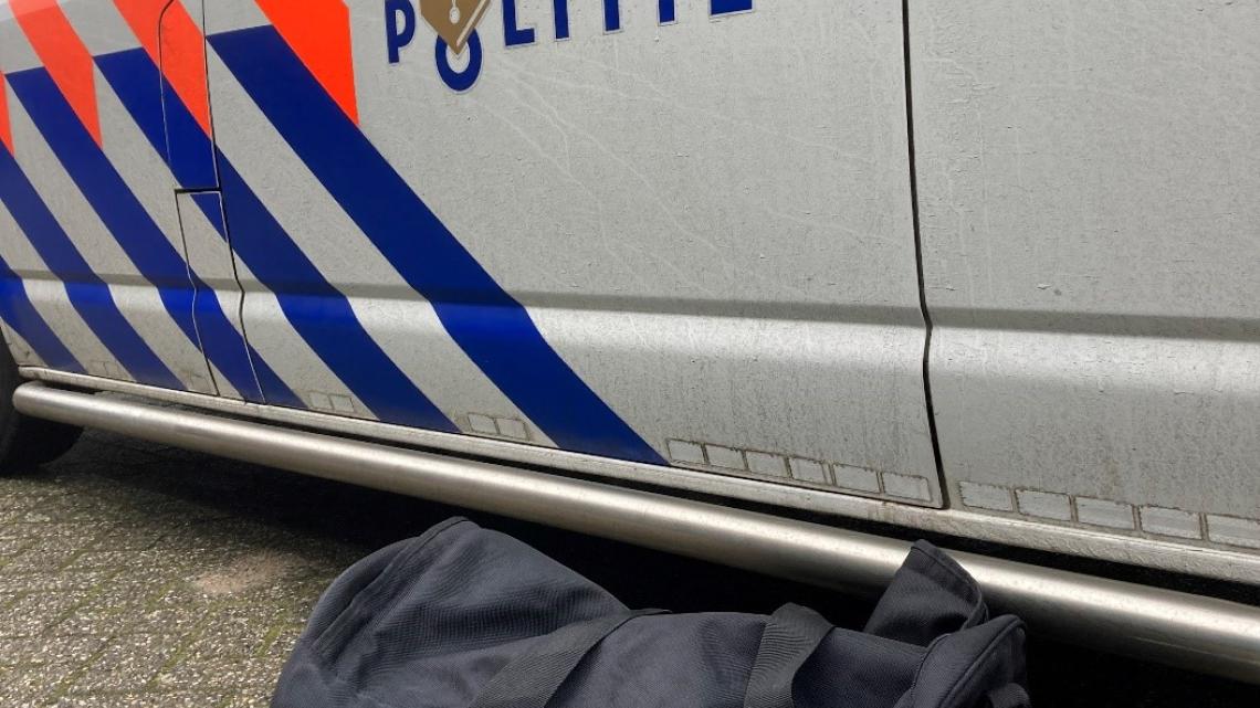 Een gesloten zwarte tas naast een politieauto